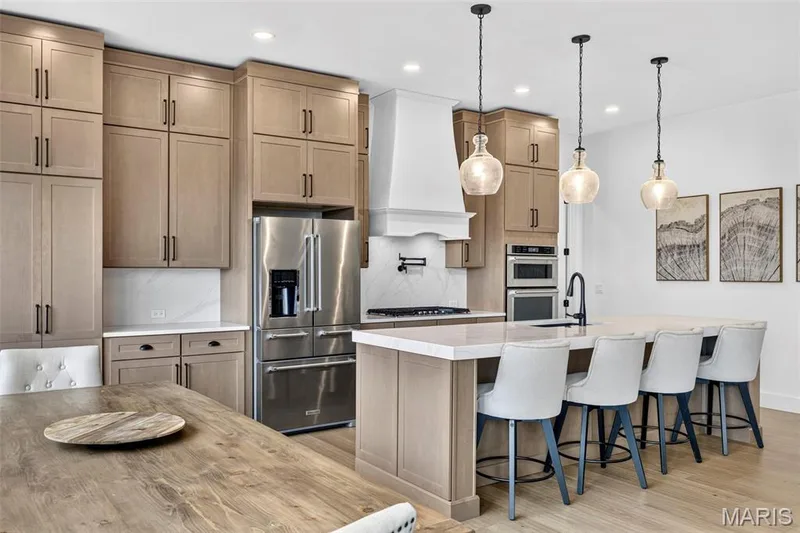 Gourmet kitchen featuring light wood-finish cabinetry, stainless steel appliances, a large center island with seating, and three pendant lights — 3 Millers Court, O'Fallon, MO 63366