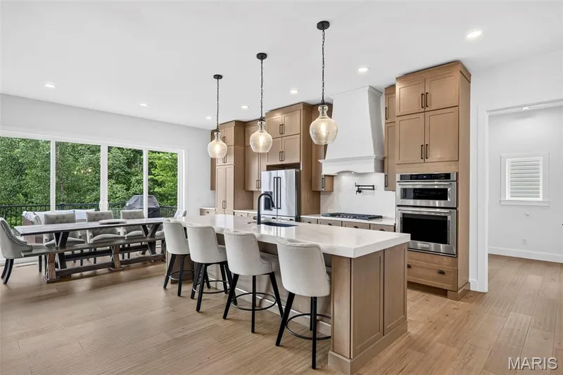 Gourmet kitchen with stainless steel appliances, custom cabinetry, a large center island with seating, and wood-finish flooring — 3 Millers Court, O'Fallon, MO 63366
