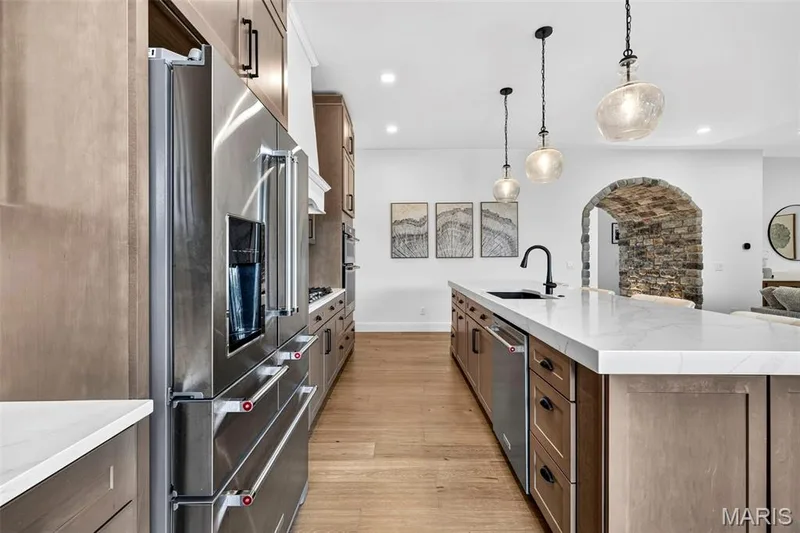 Gourmet kitchen featuring stainless steel appliances, custom cabinetry, a large kitchen island with a sink, pendant lighting, and wood-finish flooring — 3 Millers Court, O'Fallon, MO 63366