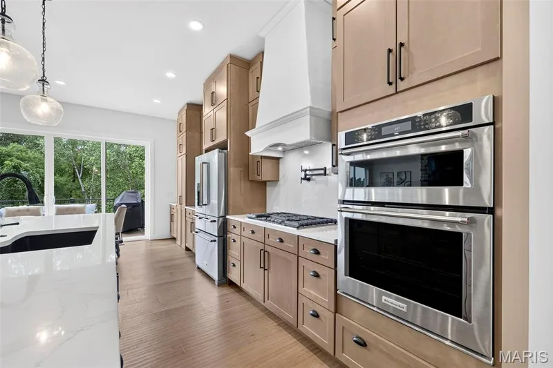 Gourmet kitchen with double wall ovens, wood-finish cabinetry, built-in refrigerator, gas cooktop, and large island with stone countertop — 3 Millers Court, O'Fallon, MO 63366