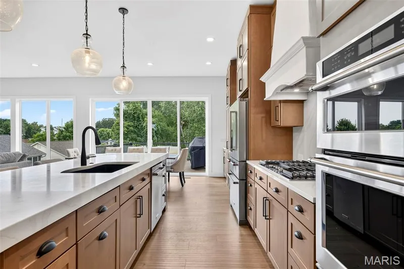 Gourmet kitchen with double wall ovens, gas cooktop, built-in refrigerator, large center island with integrated sink, and wood-finish flooring — 3 Millers Court, O'Fallon, MO 63366
