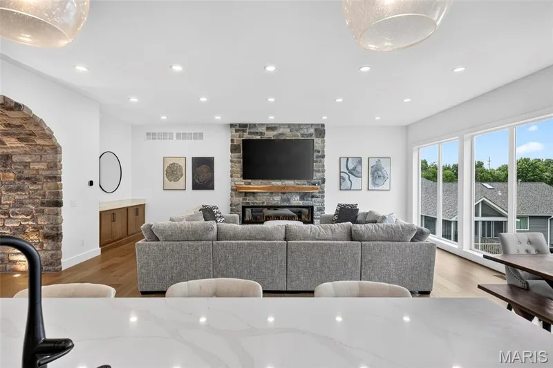 Spacious gathering room featuring a stone-clad fireplace with a wood mantle, large windows, recessed lighting, and wood-finish flooring — 3 Millers Court, O'Fallon, MO 63366