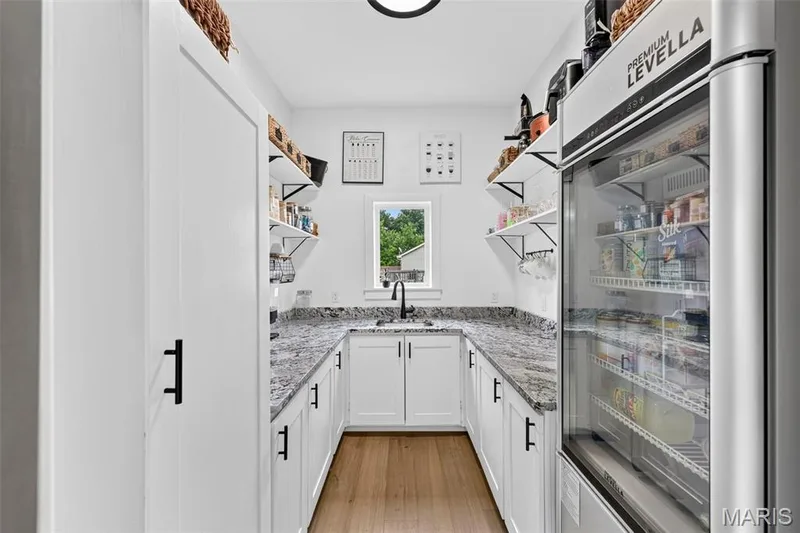 U-shaped counter space with granite countertops, wood-finish flooring, white cabinetry with black hardware, open shelving, and a built-in beverage cooler — 3 Millers Court, O'Fallon, MO 63366