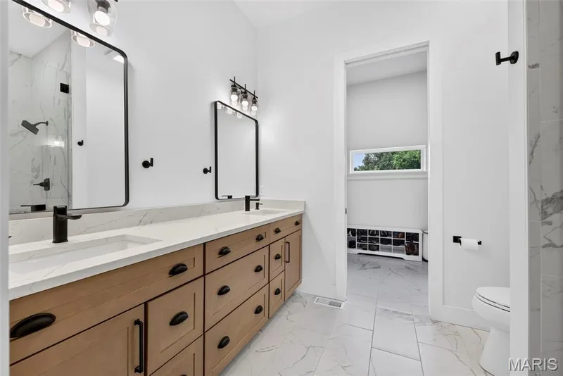 Primary Bathroom featuring a wood-finish vanity with multiple drawers and black hardware, white quartz countertop, dual framed mirrors with black metal frames, matte black faucetry, and white tile flooring — 3 Millers Court, O'Fallon, MO 63366
