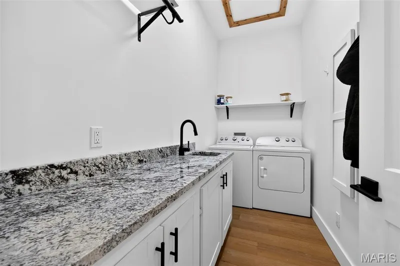 Modern laundry room featuring white cabinetry with black hardware, speckled stone countertops, a stainless steel sink with matte black faucet, and side-by-side washer and dryer appliances — 3 Millers Court, O'Fallon, MO 63366