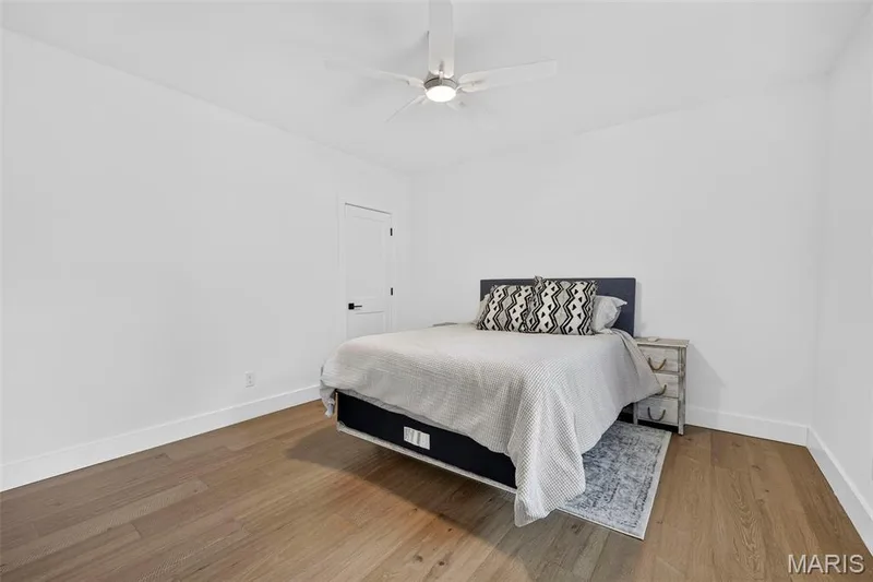 Bright bedroom showcasing warm wood-finish flooring, white walls, and a ceiling fan with integrated lighting — 3 Millers Court, O'Fallon, MO 63366