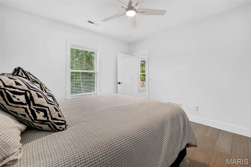 Bright secondary bedroom featuring hardwood flooring, a ceiling fan with integrated lighting, and large windows with plantation shutters providing natural illumination — 3 Millers Court, O'Fallon, MO 63366