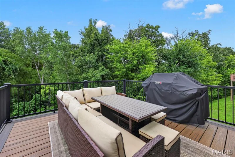 Elevated composite deck with integrated outdoor seating featuring cream-cushioned lounge furniture, wood-finish dining table, and black metal railing — 3 Millers Court, O'Fallon, MO 63366