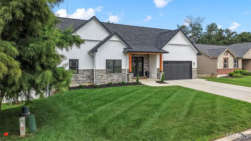 Modern farmhouse residence showcasing a clean-lined exterior with white board-and-batten siding, stone veneer accents, and a dark charcoal roof — 3 Millers Court, O'Fallon, MO 63366