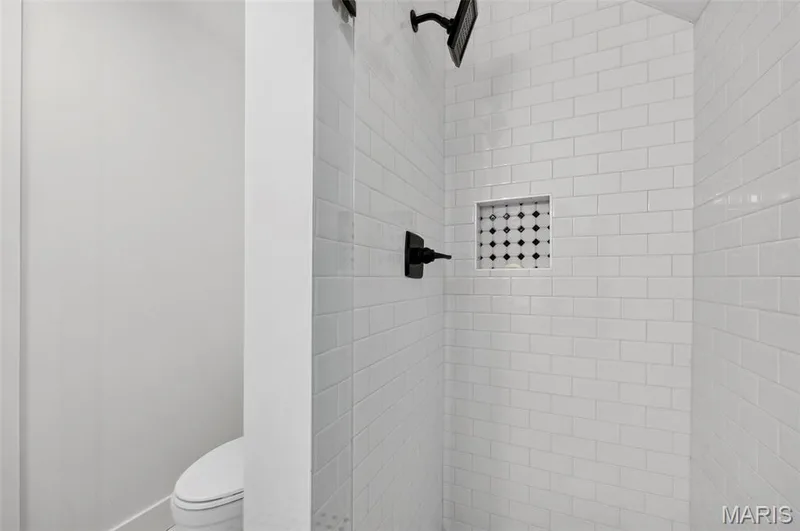 Modern bathroom featuring white subway tile walls, a recessed shelf niche with geometric tile pattern, matte black shower fixture hardware, and a clean white toilet with elongated bowl — 3 Millers Court, O'Fallon, MO 63366