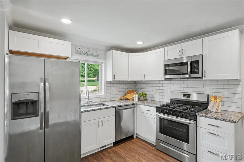 White shaker-style cabinetry, granite countertops, subway tile backsplash, wood-finish flooring, and stainless steel appliances — 31 Plackemeier, O'Fallon, MO 63366