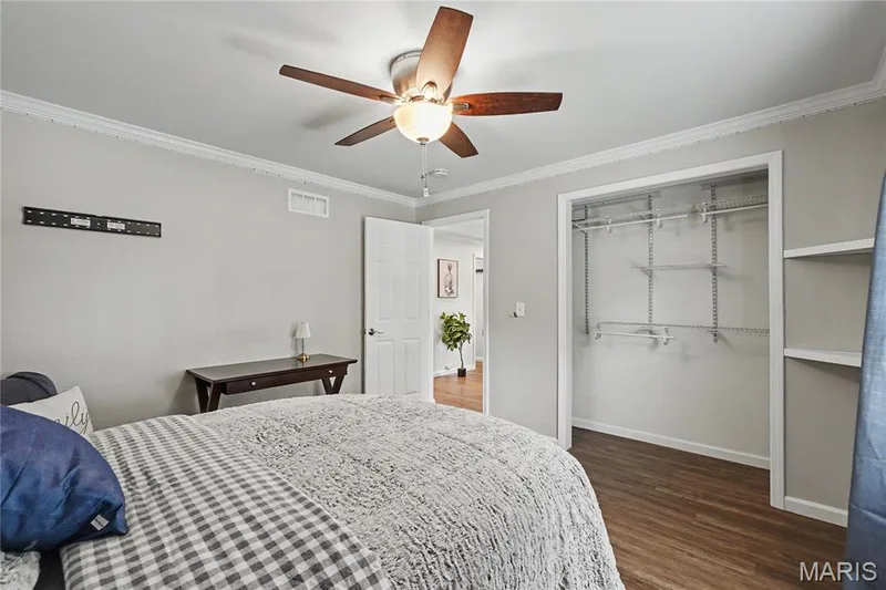 Spacious room featuring crown molding, wood-finish flooring, a ceiling fan with light fixture, and an open closet with adjustable shelving — 31 Plackemeier, O'Fallon, MO 63366