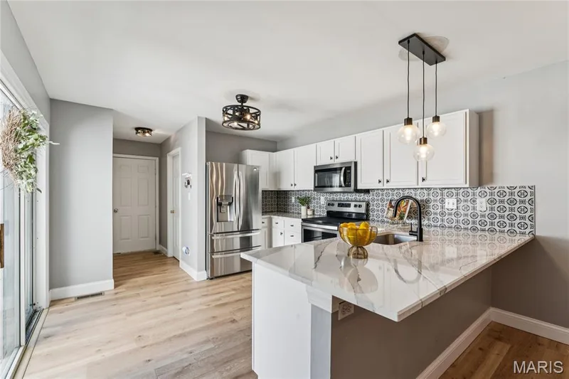 A beautifully updated kitchen takes center stage with crisp white cabinetry, stainless steel appliances, striking backsplash, and expansive countertops. Updates include: new lighting, quartz countertops, backsplash & hardware. — 947 Rolling Thunder Drive, O'Fallon, MO 63368