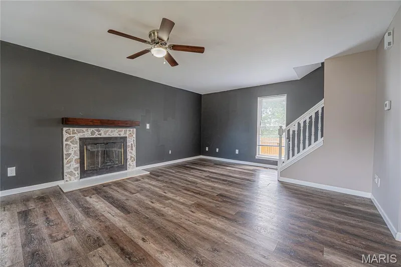 Spacious living area featuring wood-finish flooring, a ceiling fan with integrated lighting, and a stone-surround fireplace with a wood mantel — 1721 Summergate Court, St Charles, MO 63303