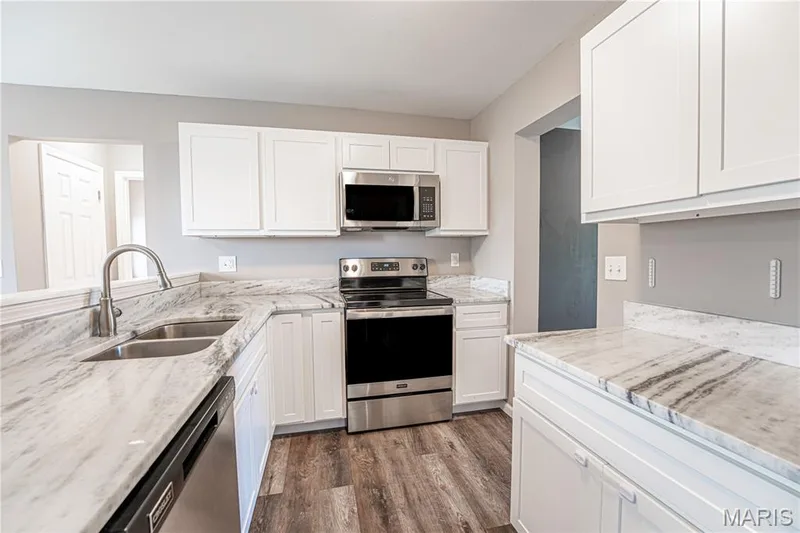 Kitchen featuring wood-finish flooring, white cabinetry, stainless steel appliances, and a double basin sink with a gooseneck faucet — 1721 Summergate Court, St Charles, MO 63303