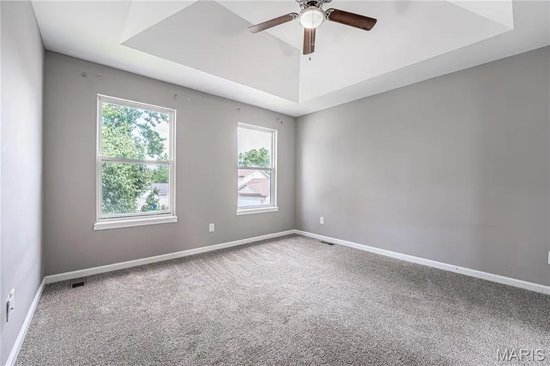 Tray ceiling with a ceiling fan, two windows, and gray carpet flooring — 1721 Summergate Court, St Charles, MO 63303