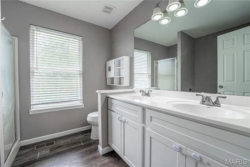 Dual vanity with integrated sinks, white cabinetry, large wall-mounted mirror, and wood-finish flooring — 1721 Summergate Court, St Charles, MO 63303