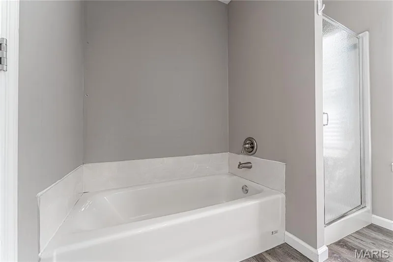 Bathtub with a shower/tub combination faucet, textured shower enclosure, and wood-finish flooring — 1721 Summergate Court, St Charles, MO 63303