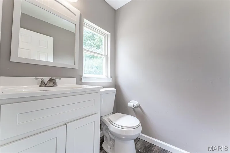 White shaker-style vanity with integrated sink, dual-pane window, toilet, and wood-finish flooring — 1721 Summergate Court, St Charles, MO 63303