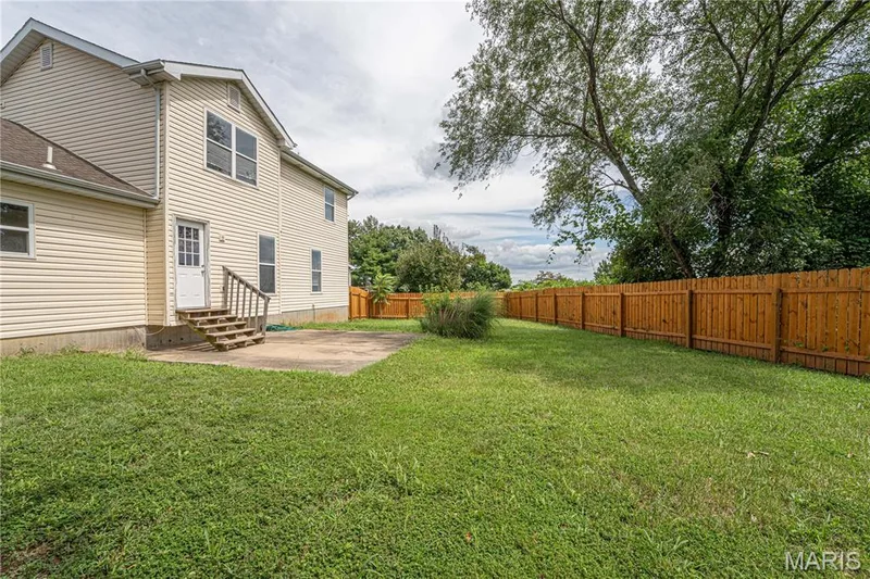 Expansive backyard with a concrete patio, wood privacy fence, and mature trees — 1721 Summergate Court, St Charles, MO 63303