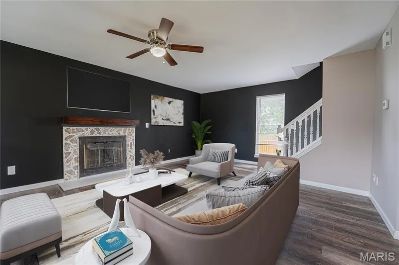 Living space featuring a stone fireplace with a wood mantel, a ceiling fan with integrated lighting, wood-finish flooring, and a staircase with white balusters — 1721 Summergate Court, St Charles, MO 63303