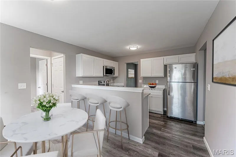 Kitchen featuring white cabinetry, stainless steel appliances, wood-finish flooring, and a breakfast bar with stone-finish countertops — 1721 Summergate Court, St Charles, MO 63303