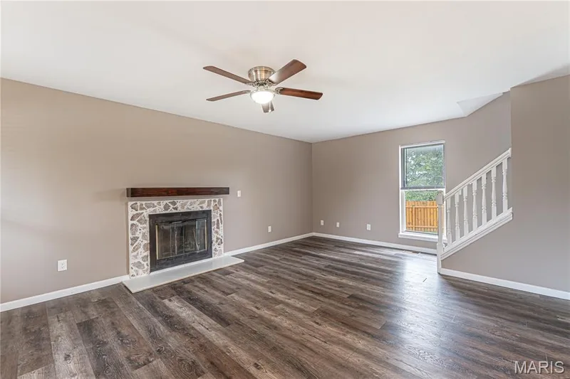 Wood-finish flooring, stone-surround fireplace with a wood mantel, ceiling fan with integrated lighting, and a white staircase with balusters — 1721 Summergate Court, St Charles, MO 63303
