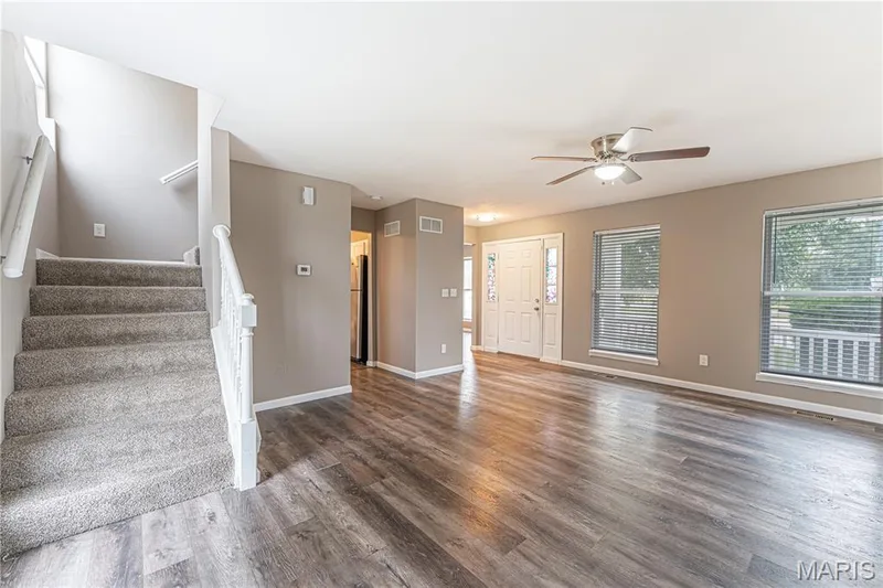 Wood-finish flooring, two large windows with blinds, a ceiling fan with integrated lighting, and a white paneled front door — 1721 Summergate Court, St Charles, MO 63303