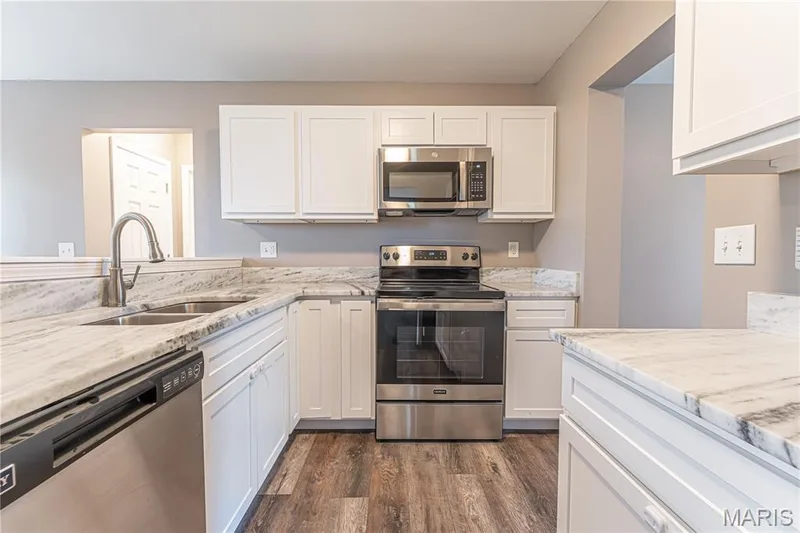 White shaker cabinetry, stainless steel appliances, dual basin sink, and wood-finish flooring — 1721 Summergate Court, St Charles, MO 63303