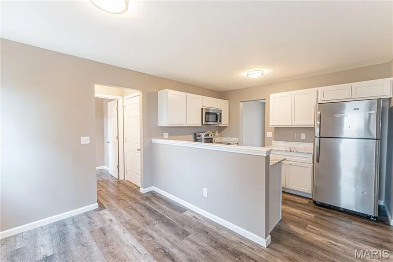 Wood-finish flooring throughout, white upper and lower cabinetry, stainless steel microwave, stainless steel refrigerator, and recessed lighting — 1721 Summergate Court, St Charles, MO 63303