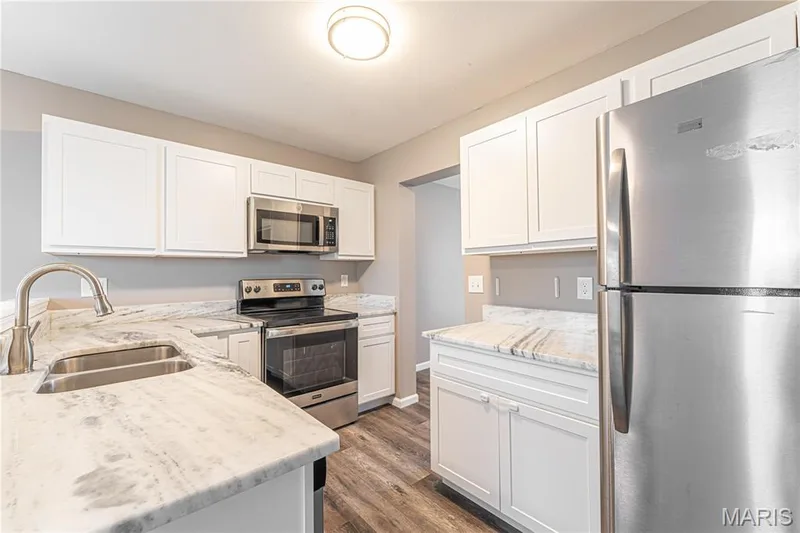Updated kitchen featuring white shaker-style cabinetry, patterned countertops, stainless steel appliances, and wood-finish flooring — 1721 Summergate Court, St Charles, MO 63303