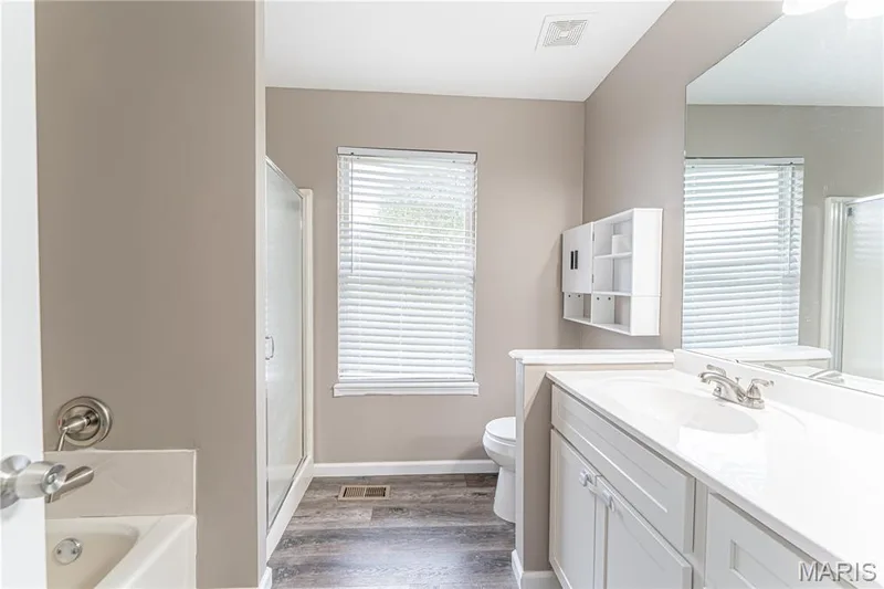 Wood-finish flooring, white vanity with dual sinks, built-in wall cabinet, shower enclosure, and soaking tub — 1721 Summergate Court, St Charles, MO 63303