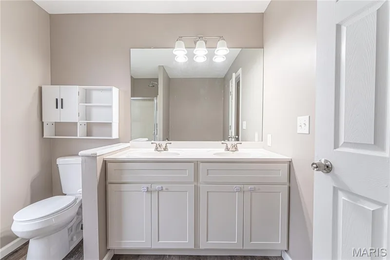 Double vanity with integrated sinks, white cabinetry, wall-mounted mirror, and overhead lighting — 1721 Summergate Court, St Charles, MO 63303