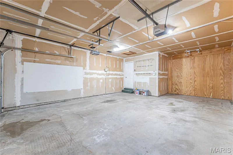Concrete flooring garage with an automatic garage door opener, overhead lighting, and wood paneling — 1721 Summergate Court, St Charles, MO 63303
