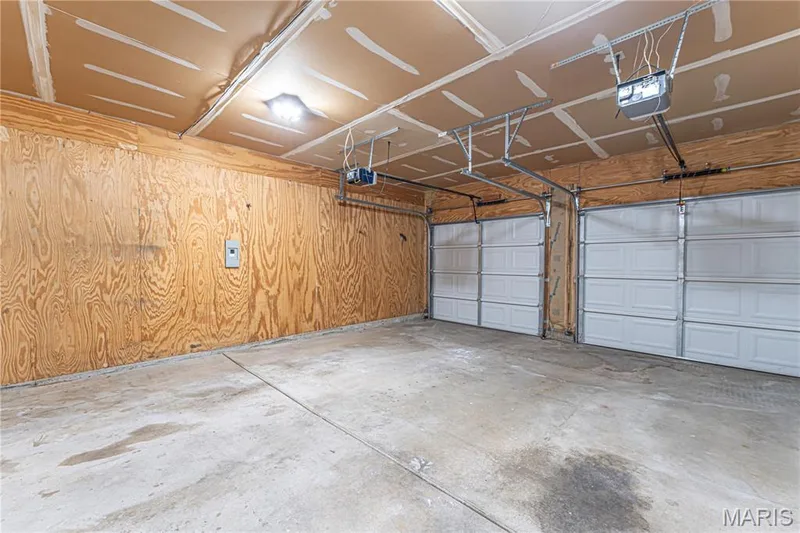 Two-car garage with concrete flooring, plywood walls, and overhead lighting — 1721 Summergate Court, St Charles, MO 63303