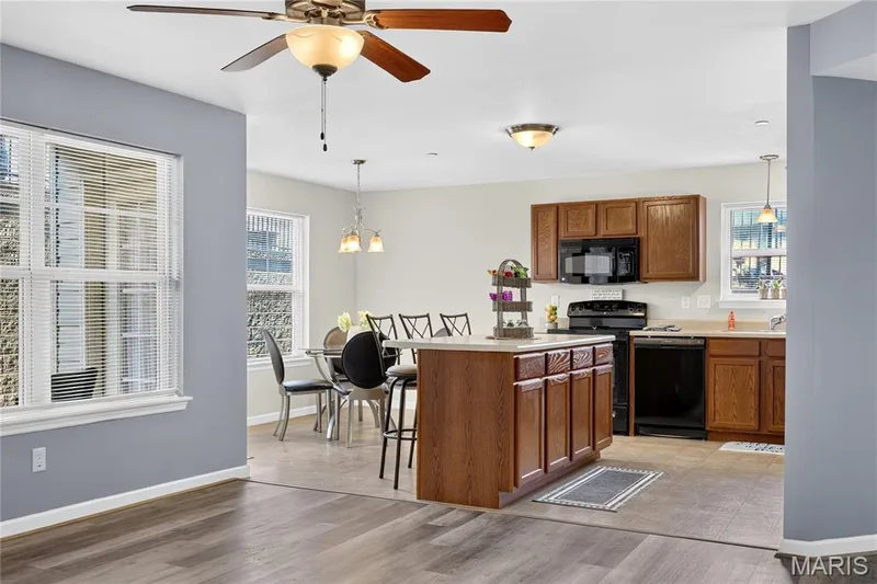 Wood-finish flooring, ceiling fan with integrated lighting, kitchen island with seating, dark wood cabinetry, and a full suite of black kitchen appliances — 313 Bramblett Hills, O'Fallon, MO 63366