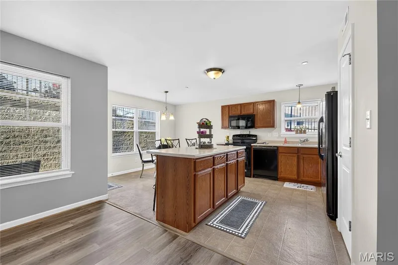 Wood-finish flooring, kitchen island with built-in cabinetry, pendant lighting, black appliances, and tile flooring — 313 Bramblett Hills, O'Fallon, MO 63366