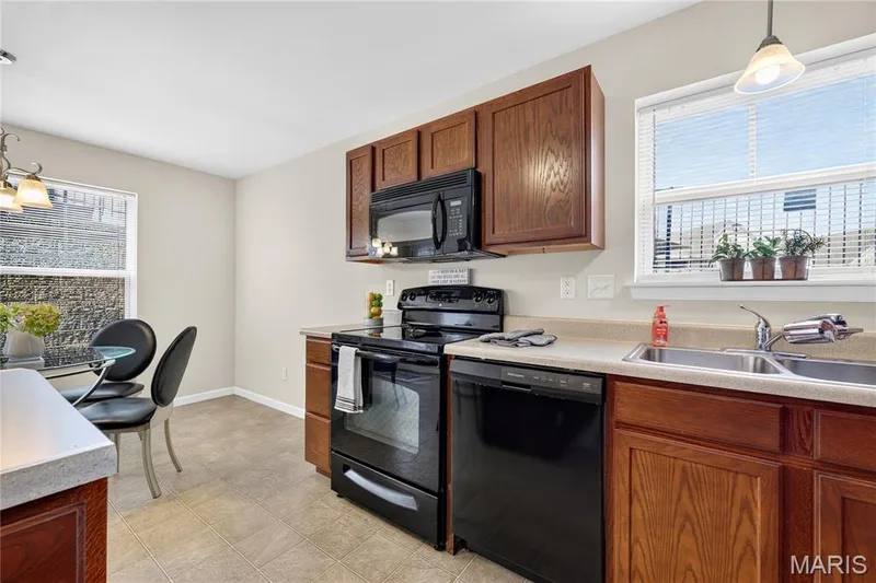 Kitchen featuring wood-finish cabinetry, black appliances, a dual basin stainless steel sink, and light-toned countertops — 313 Bramblett Hills, O'Fallon, MO 63366