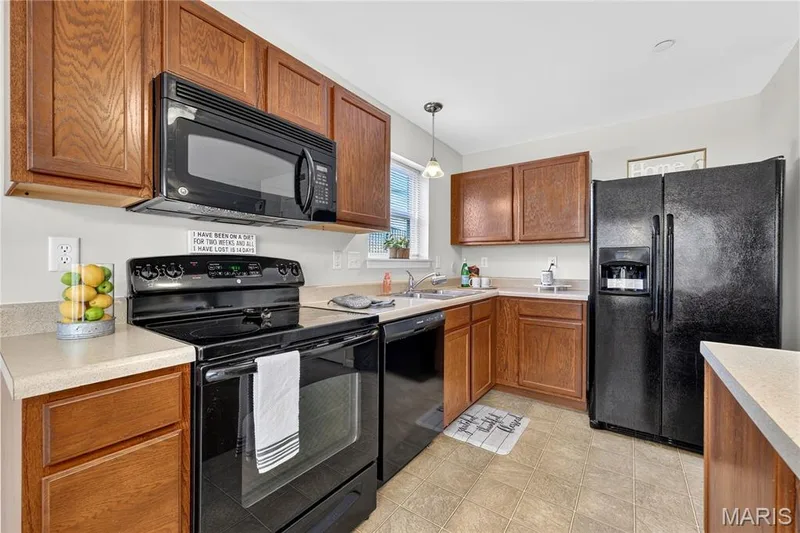 Kitchen featuring wood cabinetry, light-toned countertops, a black range, a black microwave, and a black side-by-side refrigerator — 313 Bramblett Hills, O'Fallon, MO 63366