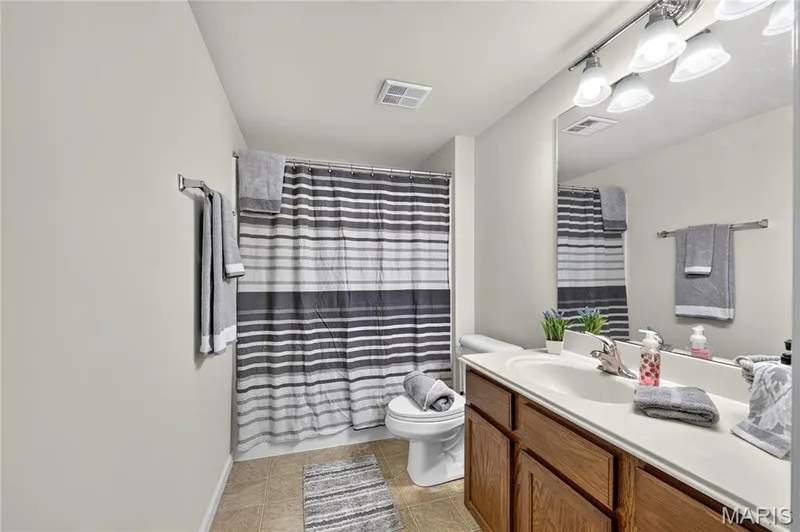 Bathroom featuring a wood-finish vanity with an integrated sink, a large wall mirror, and a track light fixture — 313 Bramblett Hills, O'Fallon, MO 63366