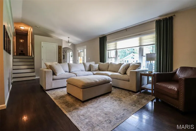 Living room boasts vaulted ceilings, dark luxury vinyl plank flooring, cozy electric fireplace, a large window with privacy shade — 12 Pyrenees Drive, Lake St. Louis, MO 63367