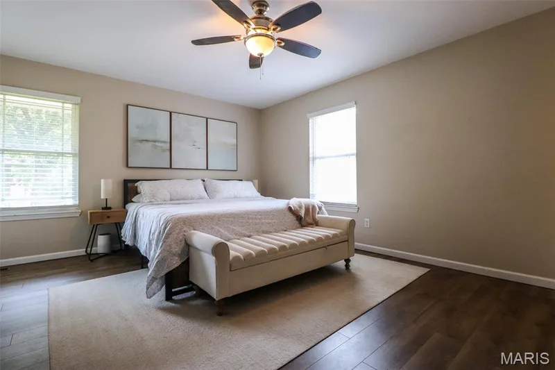 Primary bedroom boasts luxury vinyl plank flooring, ceiling fan with integrated lighting, two windows with blinds, and neutral-toned walls — 12 Pyrenees Drive, Lake St. Louis, MO 63367