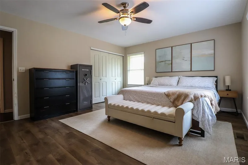 Primary bedroom boasts luxury vinyl plank flooring, ceiling fan with integrated lighting, two windows with blinds, and neutral-toned walls — 12 Pyrenees Drive, Lake St. Louis, MO 63367