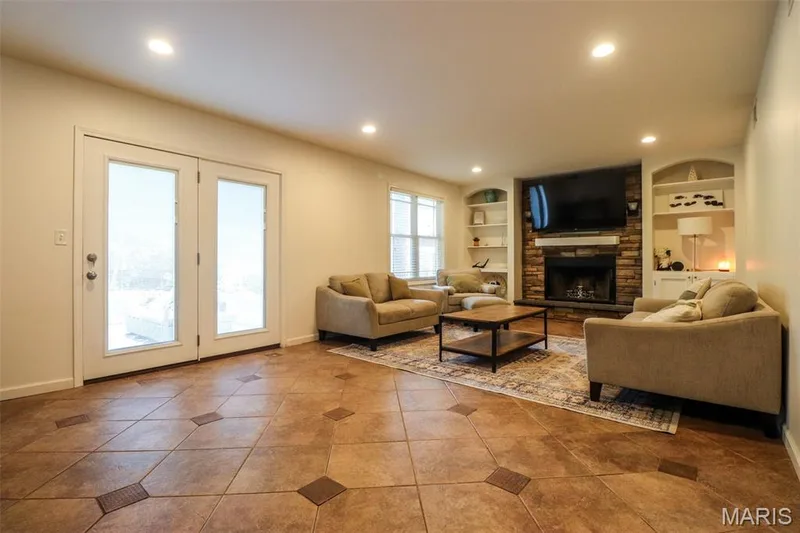 Family room with tile floors, recessed lighting, built-in shelving, wood burning fireplace, and French doors that lead to the backyard — 12 Pyrenees Drive, Lake St. Louis, MO 63367