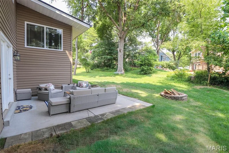 Spacious concrete patio with stone-look paver edging, a stone fire pit, and a large lawn area — 12 Pyrenees Drive, Lake St. Louis, MO 63367