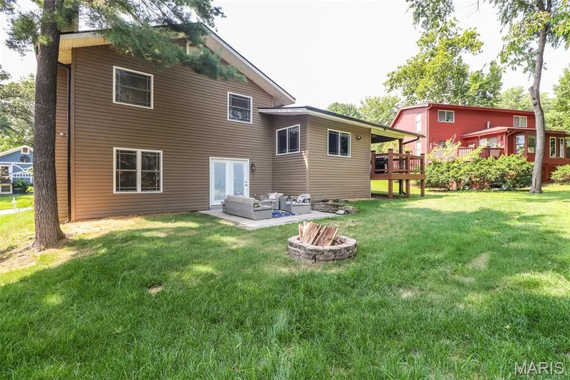 Expansive backyard featuring a stone fire pit, concrete patio, and mature trees — 12 Pyrenees Drive, Lake St. Louis, MO 63367