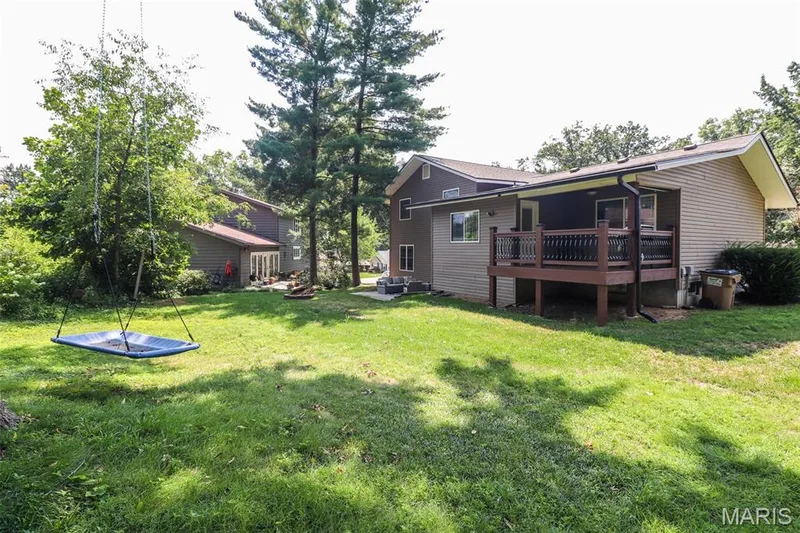 Expansive backyard featuring a stone fire pit, concrete patio, and mature trees — 12 Pyrenees Drive, Lake St. Louis, MO 63367