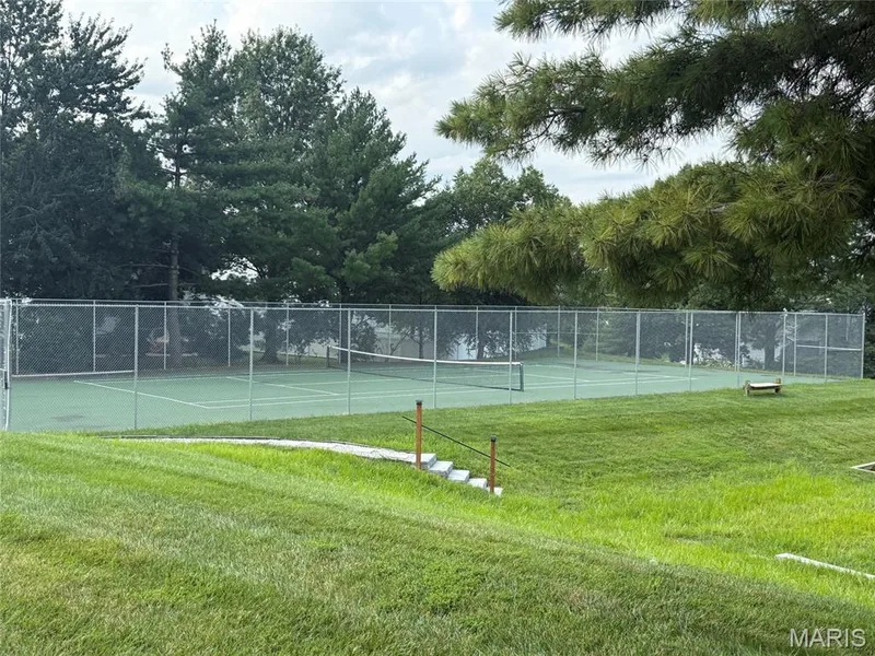 Fenced Tennis court surrounded by an expansive grassy area and mature trees — 303 Whispering Woods Drive, St Peters, MO 63304