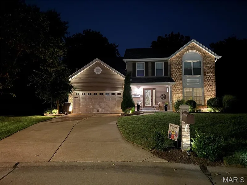 Notice the accent lighting on this beautiful two-story home featuring a brick facade, new siding, and a covered front porch — 303 Whispering Woods Drive, St Peters, MO 63304