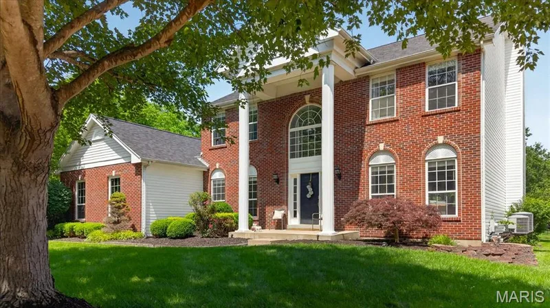 Traditional brick exterior featuring a prominent two-story portico with column supports, a large arched transom window above the main entry, and multiple multi-pane windows — 17821 Wilderness Cliff Court, Wildwood, MO 63005